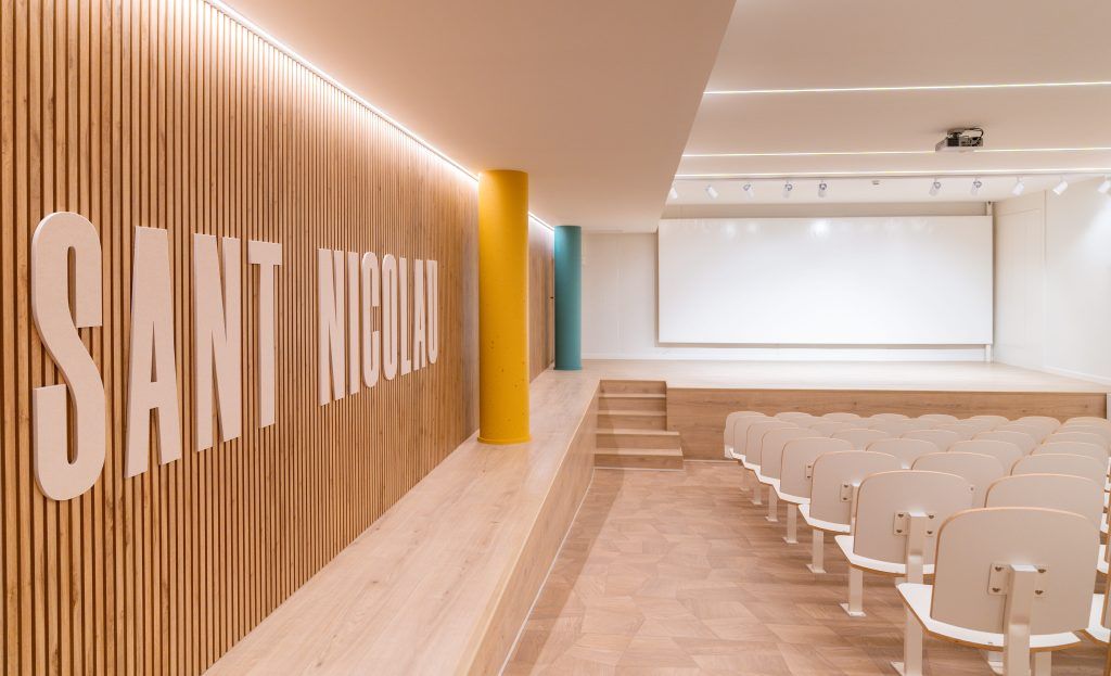 Textura y bienestar en un auditorio escolar con madera cálida y luz suave.