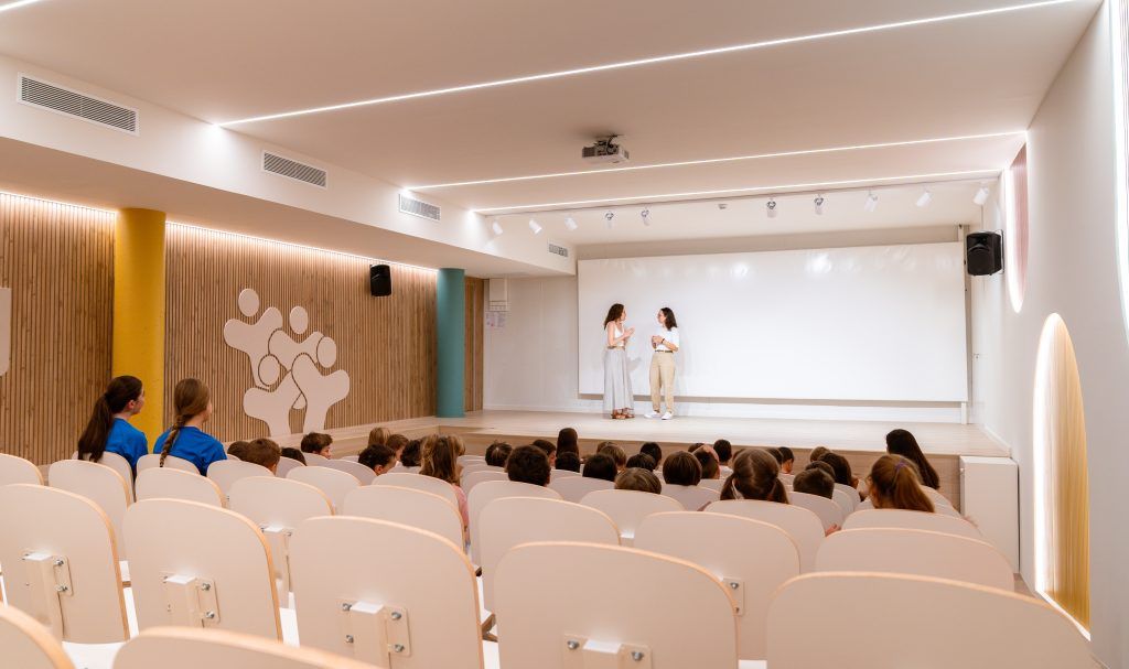 Auditorio escolar diseñado con arquitectura educativa humanizada, con iluminación cálida y materiales naturales que favorecen el bienestar del alumnado.