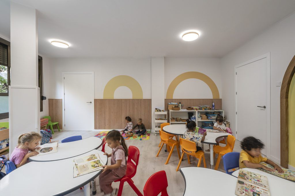 Aula infantil con mesas de trabajo y luz uniforme en el techo, ejemplo de iluminación en espacios educativos que favorece la concentración.